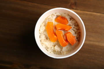 Low-calorie porridge for a healthy diet and lifestyle. Delivery to the house in a paper cup, container. Packaging made from natural materials. Barley with pieces of orange pumpkin. View from above