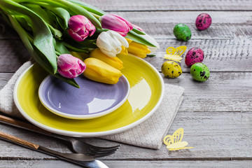 Holidays Spring Background. Easter table setting with spring tulips, colorful quail eggs and cutlery on shappy wooden background. Copy space