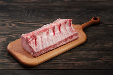 Fresh raw whole rack of pork loin with ribs on a cutting board on a dark background.