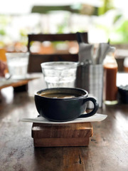 A cup of fragrant coffee with foam on a wooden stand. Background is blurred.