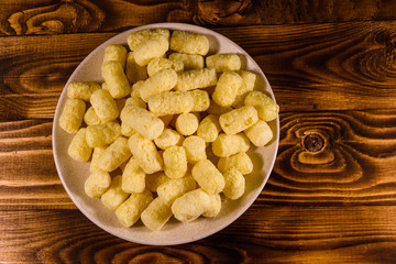 Ceramic plate with corn sticks on wooden table. Top view