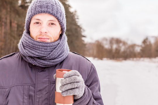 young man holds thermos in the woods in winter