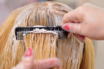 The hairdresser smears the paint on his hair with a comb, for coloring the blonde.