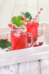 Summer homemade red currant lemonade in a mason jar with decor of berry in tray on rustic table. Close up.