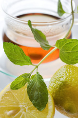 Tea in the glass cup with lemon and fresh mint leaves - herbal healing tea as homemade remedy