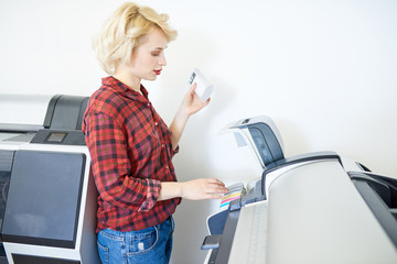 Side view portrait of modern young woman loading printers with ink in publishing company, copy space