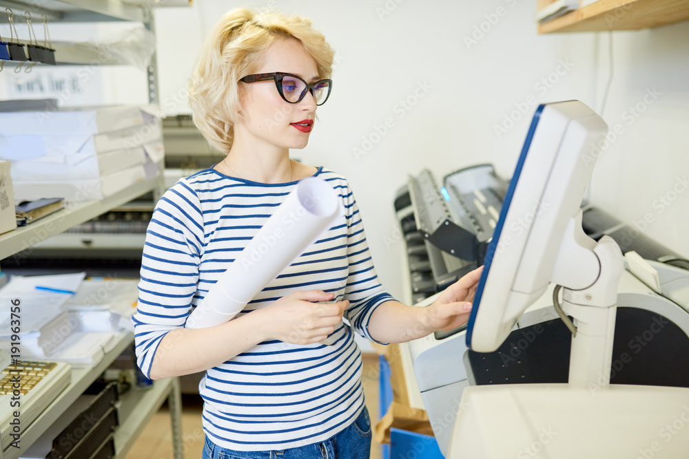 Poster portrait of blonde young woman using plotter machine operating it via computer while working in mode