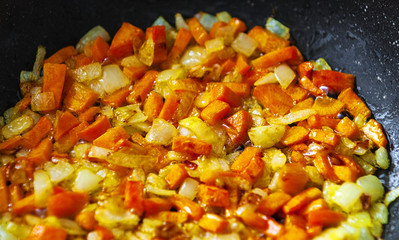 Chopped onions and carrots fry in vegetable oil in a frying pan on a black