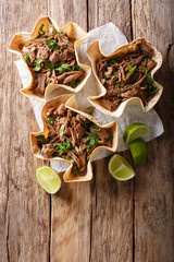 Pulled beef with lime and greens in a corn tortillas close-up on a table. Vertical top view