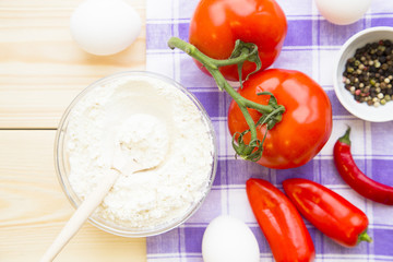 Cooking concept - red and yellow pappers, flour and tomatos on wooden table. Set of healthy food products are sources of vitamins and minerals. Closeup