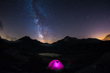 Fototapeta na wymiar Camping under starry sky and milky way at high altitude on the Alps. Illuminated tent in the foreground and majestic mountain peak in the background. Adventure and exploration in summertime.