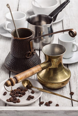 White cups for coffee of different shapes and three coffee makers. Grain of coffee and spoon on saucer.
