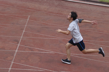 Side view of athletic handsome young Asian runner sprinter crossing the finish line on track in stadium.