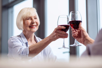 For you. Selective focus of glass of wine carried by sincere kind mature woman who smiling and wearing shirt