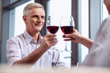 Be healthy. Happy merry mature man rising glass of wine while gazing straight and grinning