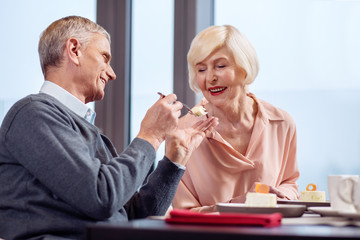 Sweet date. Handsome cheerful mature man sharing desert with wife while smiling and having date