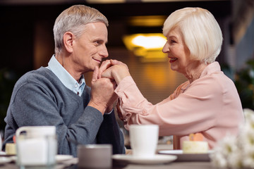 Forever yours. Pleasant handsome mature man lipping wife hand and looking at her while smiling