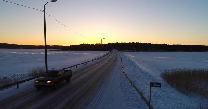Car on a winter bridge, Cinema 4k aerial rising view of a truck car on a frozen archipelago bridge, on a sunny winter evening dawn, in sarkisalo, Varsinais-suomi, Finland