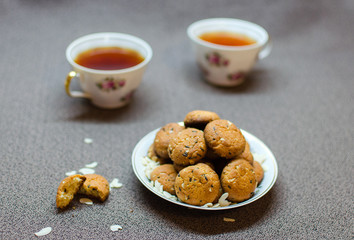 Chocolate and peanut cookies on plate with two cups of tea on brown background