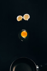 close up view of raw egg yolk falling on frying pan isolated on black
