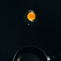 close up view of raw egg yolk falling on frying pan isolated on black