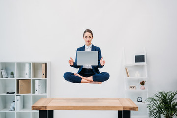 businesswoman using laptop while levitating in office - obrazy, fototapety, plakaty