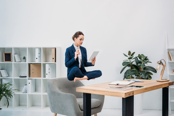 businesswoman using digital tablet while levitating at workplace - obrazy, fototapety, plakaty