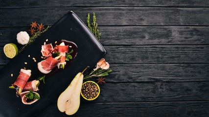 Prosciutto with pear and berry sauce. Cold snacks. Top view. On a black wooden background. Copy space.