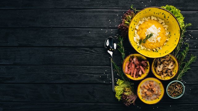 Banosh with cheese, bacon, mushrooms and lard. Hot appetizers. Top view. On a black wooden background. Copy space.
