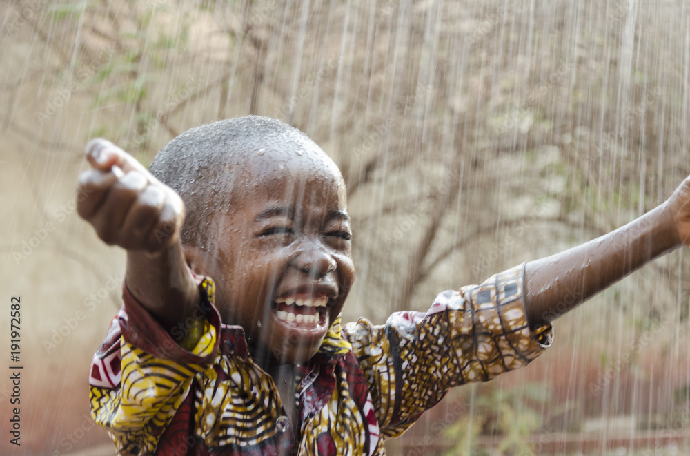 Wall mural little native african boy standing outdoors under the rain (water for africa symbol)