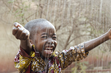 Little Native African Boy Standing Outdoors Under the Rain (Water for Africa Symbol) - obrazy, fototapety, plakaty