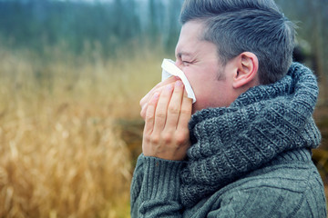 blond man outdoors blowing his nose