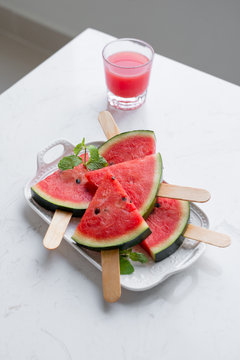 Fresh red smoothie in a glass with sliced pieces of watermelon on table.