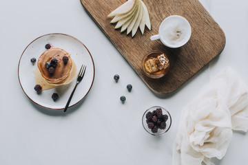 top view of tasty healthy pancakes with berries and cup of cappuccino on grey