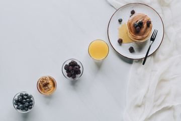 top view of tasty breakfast with pancakes, berries, honey and juice on grey