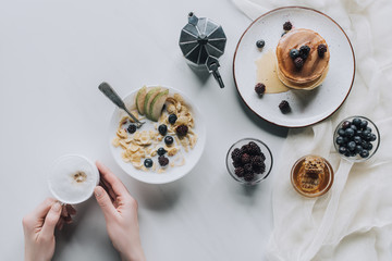 cropped shot of person holding cup of cappuccino while having tasty breakfast