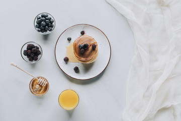 top view of sweet tasty pancakes with honey, berries and juice on grey