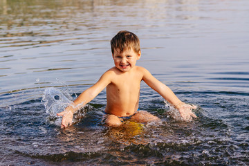 little boy splashes water . Swimming in warm lake on Sunny summer day