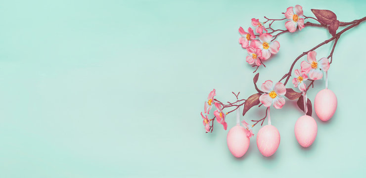 Easter border with hanging pastel pink Easter eggs and spring blossom at light at blue turquoise background.
