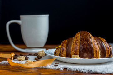Coffee cup with a croissant on vintage wooden table.