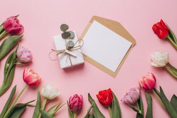 Gift and card on a pink background with tulips. Flat lay and top view.
