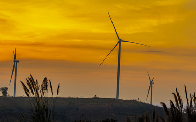 Silhouette wind turbine farm over moutain with orange sunset and cloud in blue twilight sky