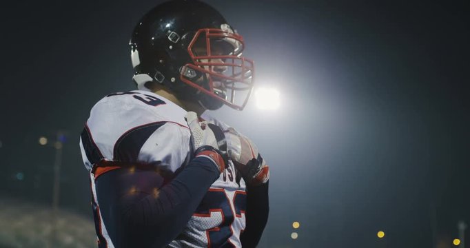 American football player putting on his protective accesories against bright stadium illumination lights