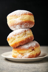 A stack of three sufganiyot donuts with jelly on black background