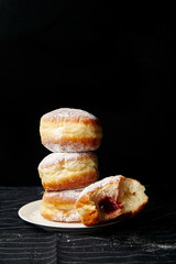 A stack of three sufganiyot donuts with jelly on black background