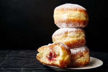 A stack of three sufganiyot donuts with jelly on black background - obrazy, fototapety, plakaty