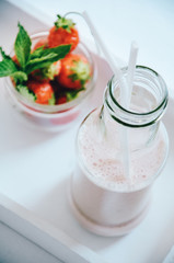 Strawberry milkshake in glass bottle with drinking straw garnished with fresh strawberries on white background