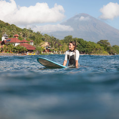 Fototapeta na wymiar sportswoman sitting on surf board in ocean, coastline on background