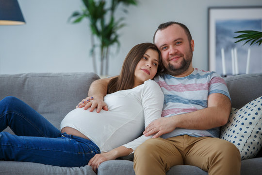 Photo of happy pregnant woman and man on gray sofa