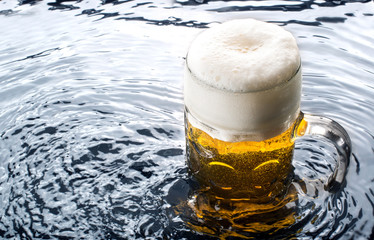 frisch gezapftes Bier im Maßkrug mit hellem Schaum steht in kühlem Wasser